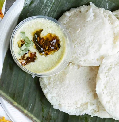 Idli with a cup of coconut chutney on banana leaf