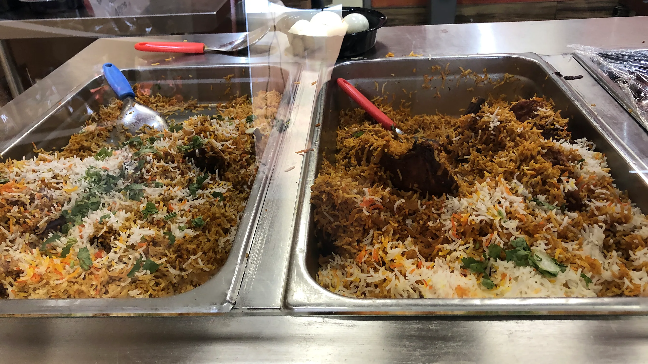 Two steel trays of fresh biryani with herbs on the hot counter