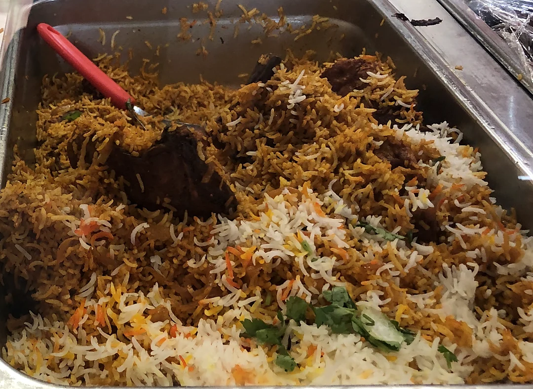 Tray of biryani with pieces of meat and fresh coriander